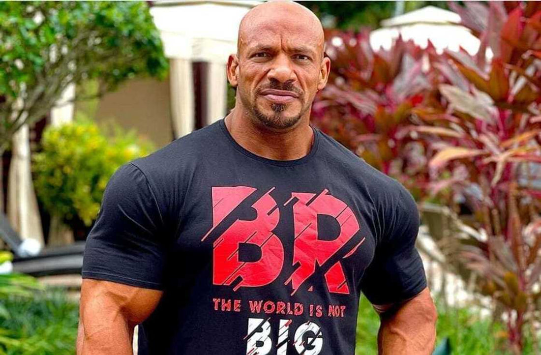 Big Ramy standing outdoors in a black shirt, his broad shoulders and muscular arms clearly visible