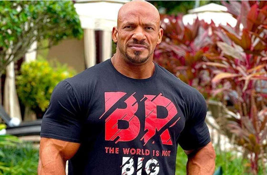 Big Ramy standing outdoors in a black shirt, his broad shoulders and muscular arms clearly visible
