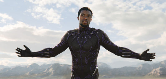 Chadwick Boseman as T'Challa wearing the black and purple Black Panther suit against a bright sky