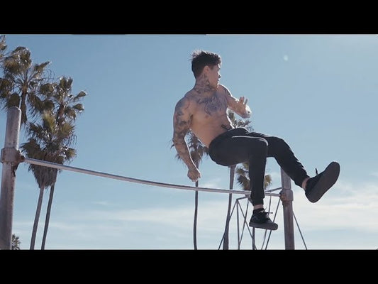 Chris Heria demonstrating an advanced bodyweight bar skill outdoors at Venice Beach