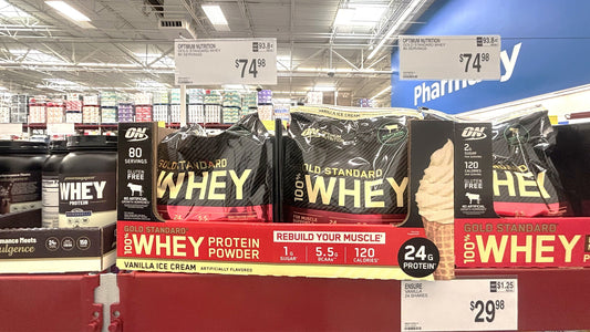 Retail whey protein tubs displayed beneath price signs in a supplement aisle