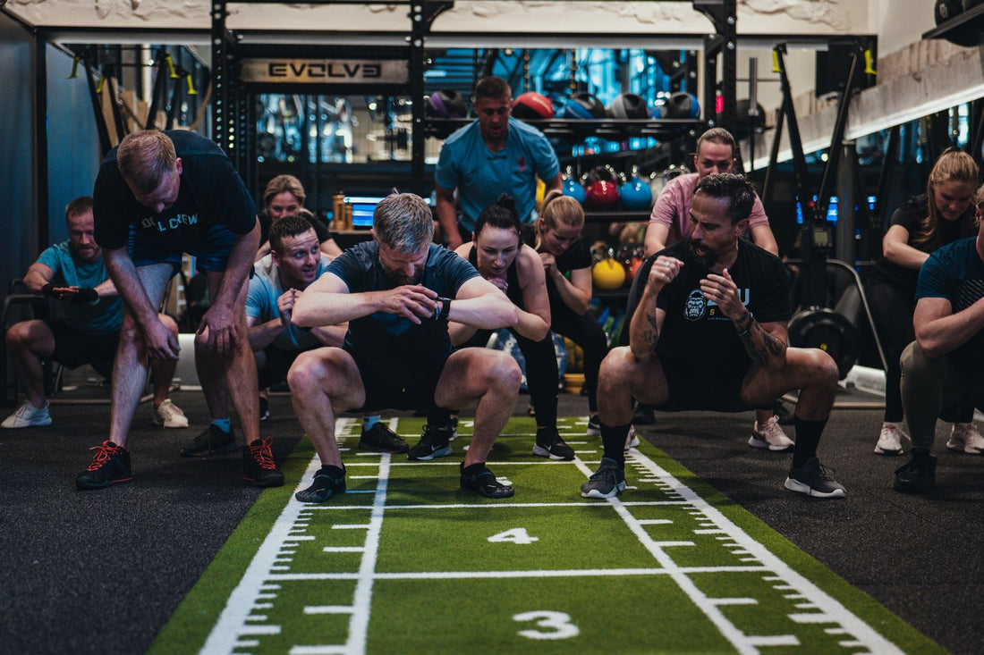Group of gym members performing deep bodyweight squats on indoor turf
