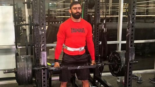 Eric Bugenhagen standing with a heavily loaded barbell inside a weight-training facility