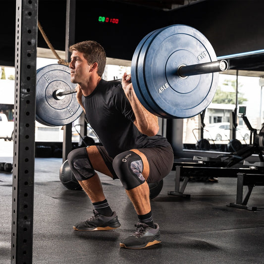 Athlete wearing knee sleeves while performing a barbell back squat in a gym