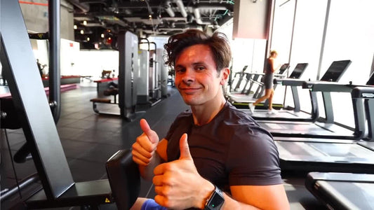 Will Tennyson smiling and giving two thumbs up while seated in a modern gym