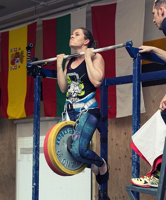 Female streetlifting athlete performing a heavy weighted pull-up in competition