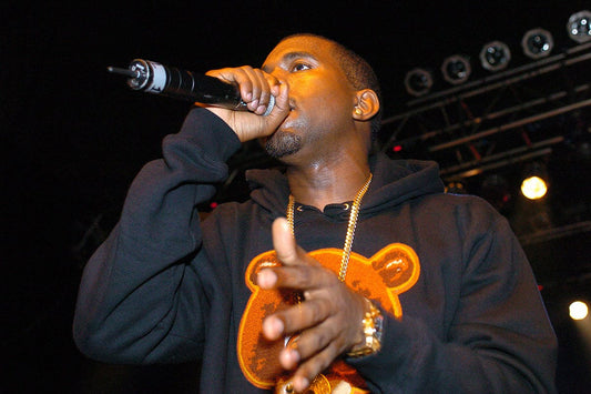 Kanye West performing onstage in a black hoodie featuring a College Dropout bear graphic