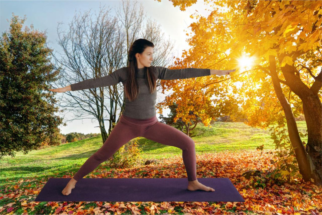 An athlete practicing yoga in an autumn park with arms extended in a grounded standing pose