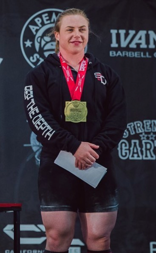 Female powerlifter celebrating with a gold medal after a strength competition
