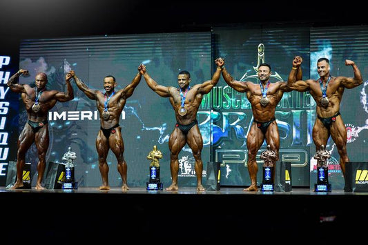 Five Classic Physique competitors celebrate on stage with medals and trophies at the 2026 Mr. Olympia Brasil Expo in São Paulo