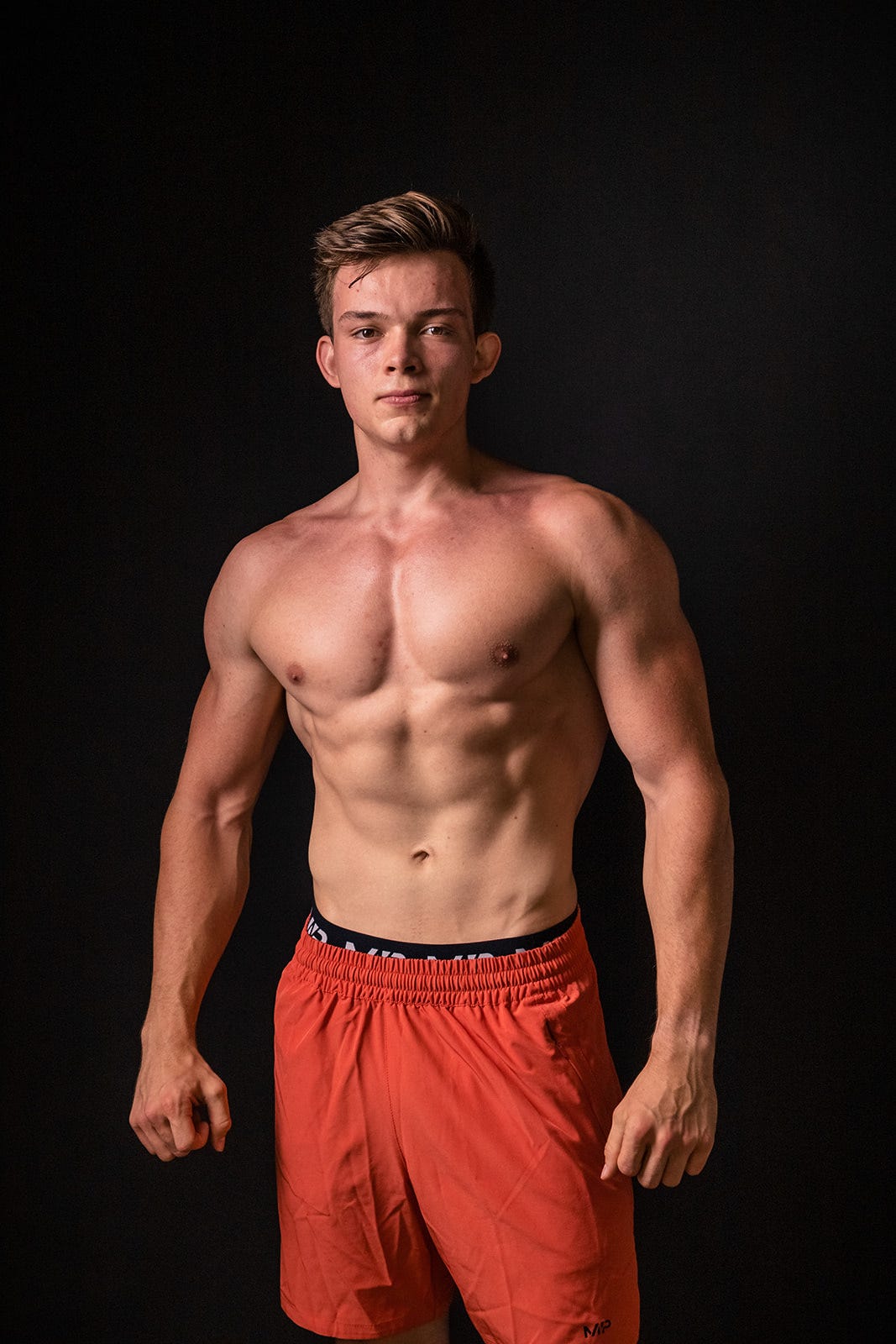 Browney posing with a lean, muscular upper body against a dark studio background
