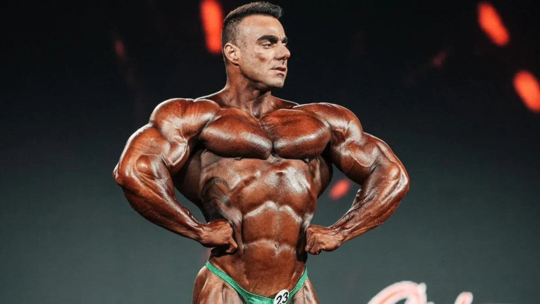 Rafael Brandao posing on a bodybuilding stage in green trunks, showing a muscular V-taper and defined chest