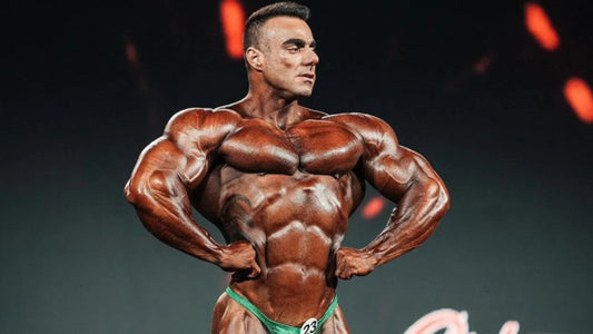 Rafael Brandao posing on a bodybuilding stage in green trunks, showing a muscular V-taper and defined chest