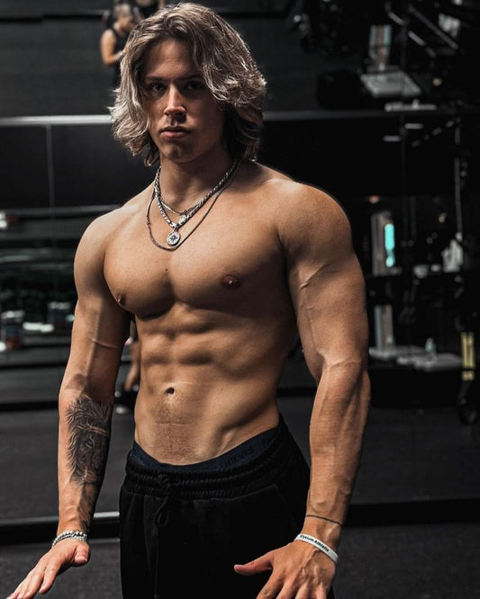 Alex Eubank shirtless in a gym showing developed chest, shoulders and abs under dark lighting