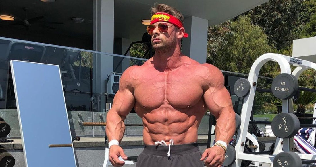 Joey Swoll posing shirtless with a muscular chest at an outdoor gym