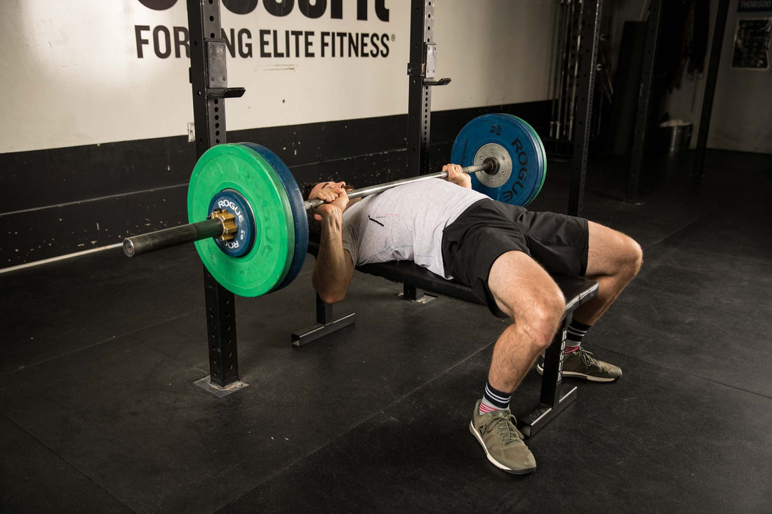 CrossFit athlete bench pressing a loaded barbell during the Linda benchmark workout