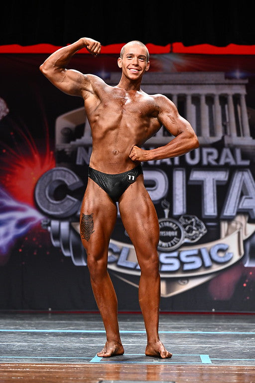 Natural bodybuilder posing on a competition stage ahead of a Classic Physique contest