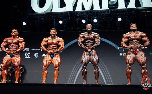 Male physique competitors posing in a bodybuilding stage lineup at an illustrative competition, not the Bradford 2026 show