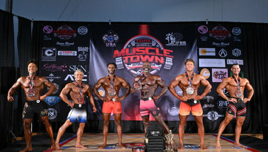 Athletes posing beneath the York Barbell Muscletown Natural Pro banner at a physique competition
