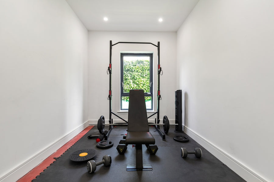Compact home gym with adjustable bench, dumbbells, rubber flooring and a rack in a bright dedicated room