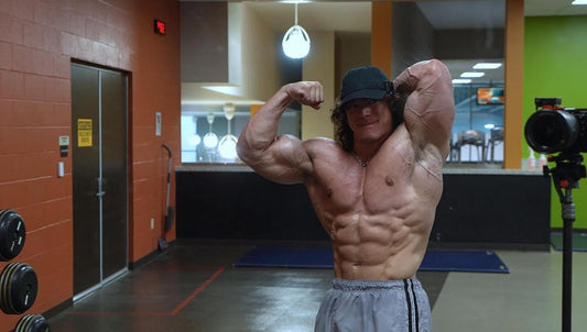 Sam Sulek curling a dumbbell in a gym, wearing a black cap and T-shirt