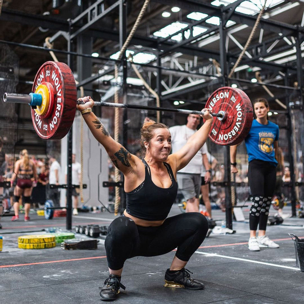 Female athlete receiving a barbell overhead in a deep squat during a CrossFit workout.