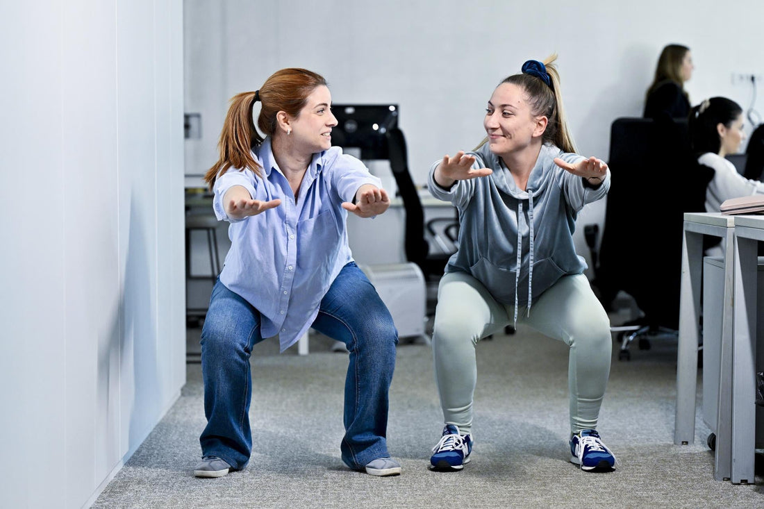 Two office workers performing bodyweight squats together during a movement break