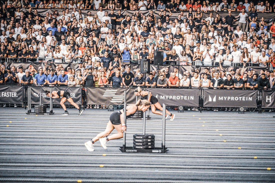 HYROX athletes push heavy weighted sleds in parallel lanes at a crowded indoor championship