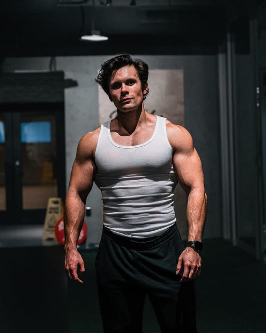 Will Tennyson standing in a white tank top in a dimly lit gym