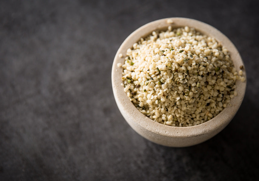 A ceramic bowl filled with pale hulled hemp seeds on a dark background
