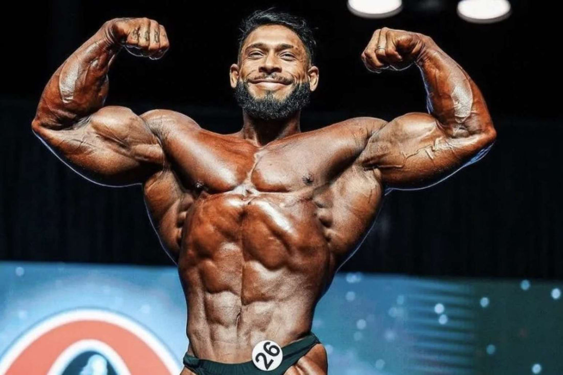 Ramon Dino flexing his biceps onstage in black Classic Physique posing trunks