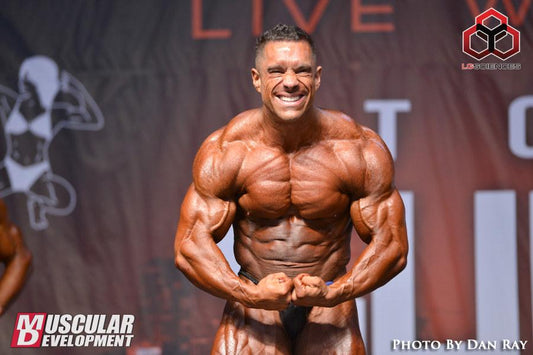 Greg Doucette posing in a gym with defined chest, arms and abdominal muscles