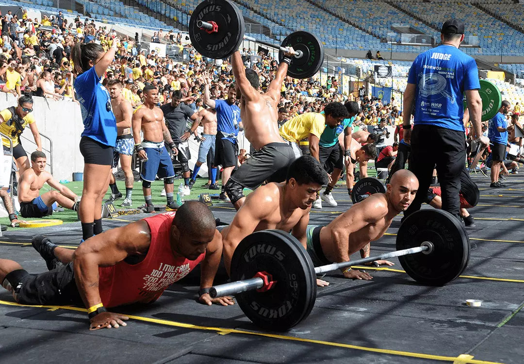 CrossFit competition athletes performing burpees and overhead barbell lifting on a stadium floor