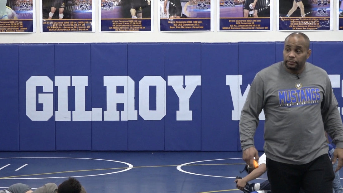 Daniel Cormier demonstrates a wrestling takedown defense in a blue training shirt as young athletes watch at camp.
