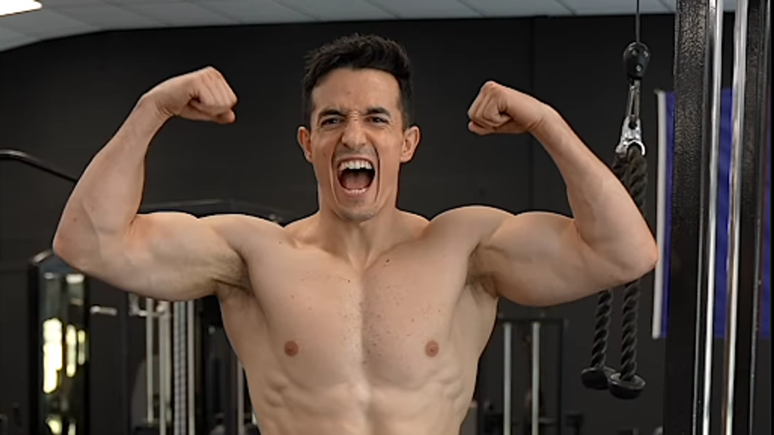 Tibo InShape flexing his arms and showing his muscular upper body in a gym