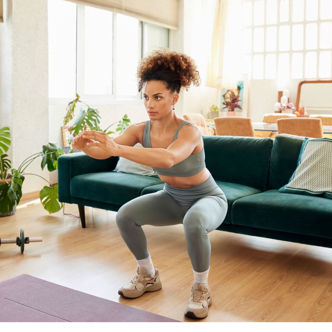 A woman performing a bodyweight squat in a bright home workout space