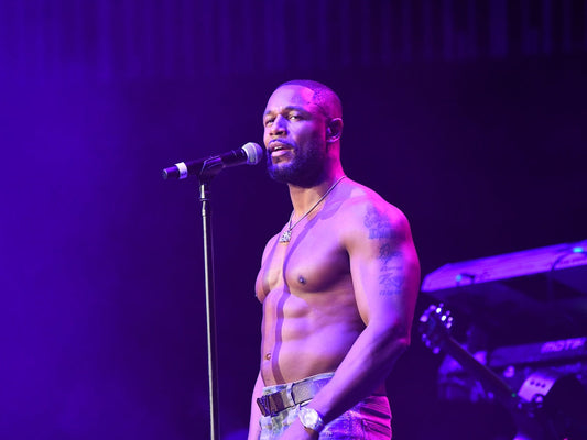R&B singer Tank performing shirtless under purple stage lights, microphone in front of him