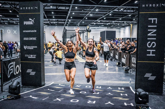 Two HYROX Doubles athletes celebrating together at an indoor race finish line