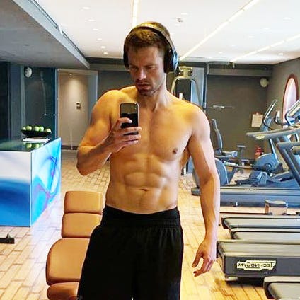 Sebastian Stan performs a shirtless triceps dip during a fitness photo shoot, showing his lean muscular upper body