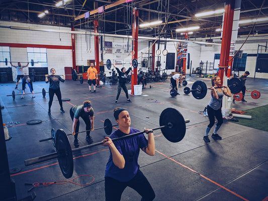 CrossFit athletes training with barbells in a large functional fitness gym
