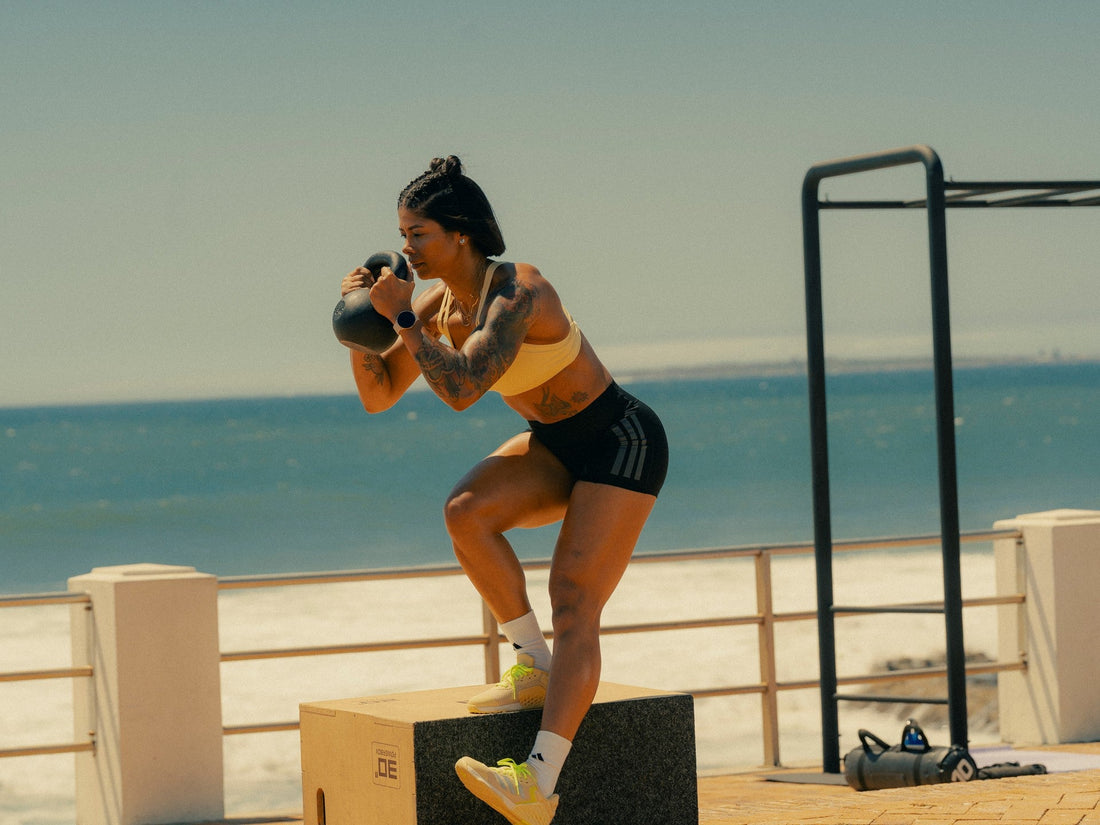 Massy Arias performing a kettlebell step-up during an outdoor athletic strength session beside the sea