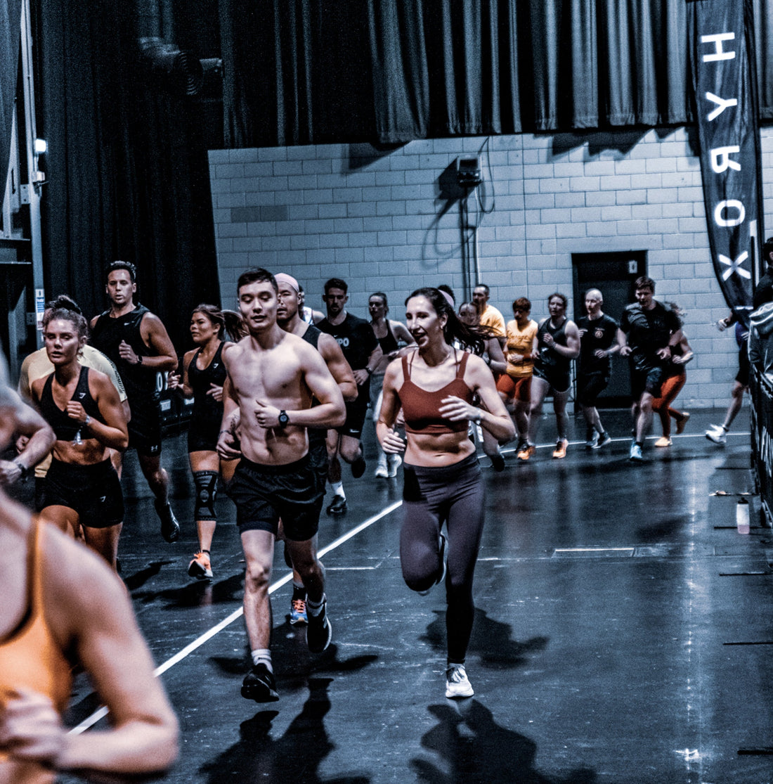 HYROX competitors running together through an indoor race course between functional fitness stations