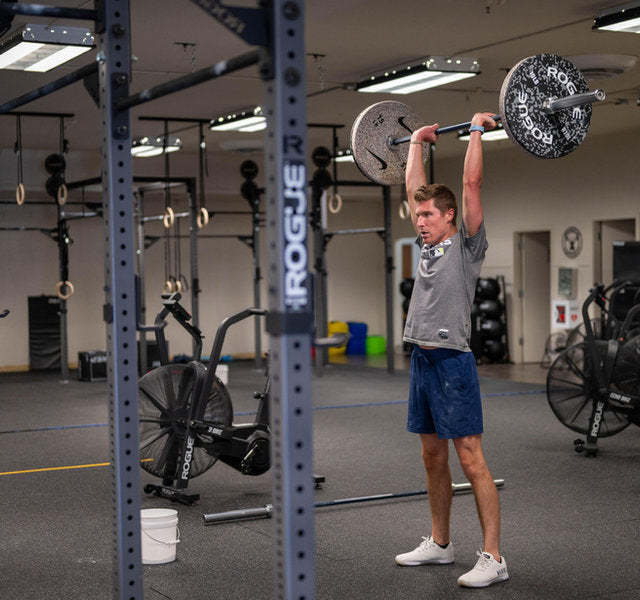 Functional fitness athlete locking out a barbell overhead