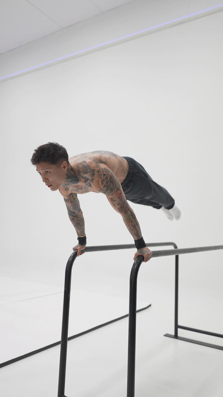 Chris Heria demonstrates a full planche with his body horizontal above parallettes