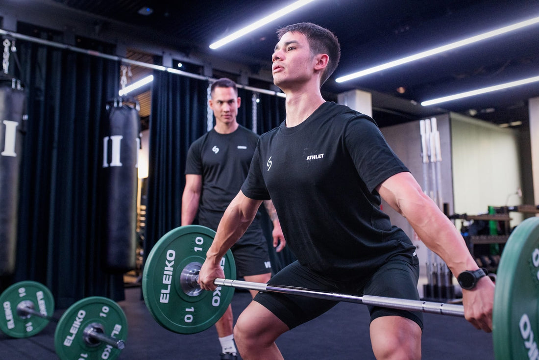 Athlete practicing a barbell lift under a coach's supervision in a strength gym