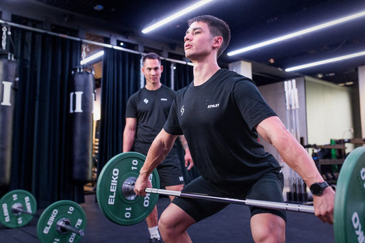 Athlete practicing a barbell lift under a coach's supervision in a strength gym