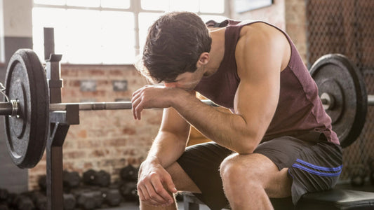 Exhausted male weightlifter sitting on a gym bench with his head lowered after training