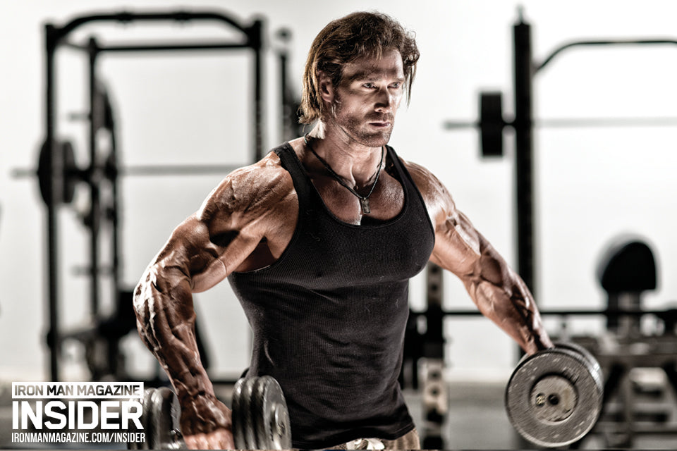 Mike O'Hearn training his shoulders in a black tank top at the gym