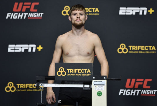 An MMA athlete stands shirtless at the official weigh-in scale in front of UFC branding
