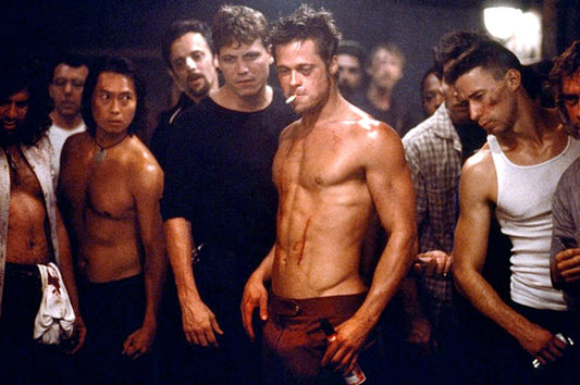 Brad Pitt as Tyler Durden standing shirtless in the underground Fight Club, showing defined chest and shoulders